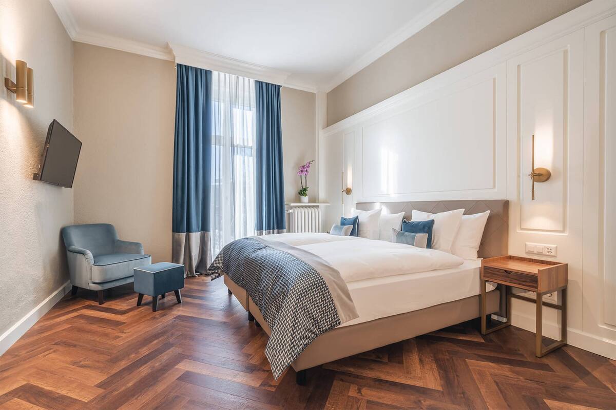 A bedroom with a large bed, a chair, a small table, and a TV mounted on the wall.