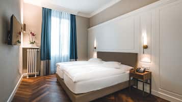 A hotel room with a large bed, a bedside table with a phone, a radiator, and a mirror on the wall.