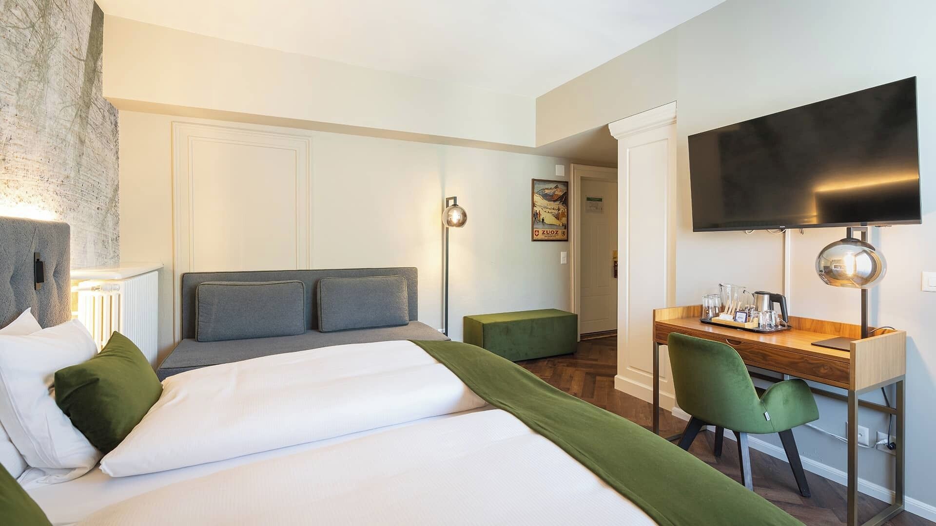 A hotel room with a bed, a desk, a chair, a flat-screen TV, and a painting on the wall.