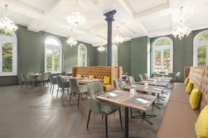 Uma ampla sala de jantar com pé direito alto, lustres e grandes janelas que oferecem vista para o verde.