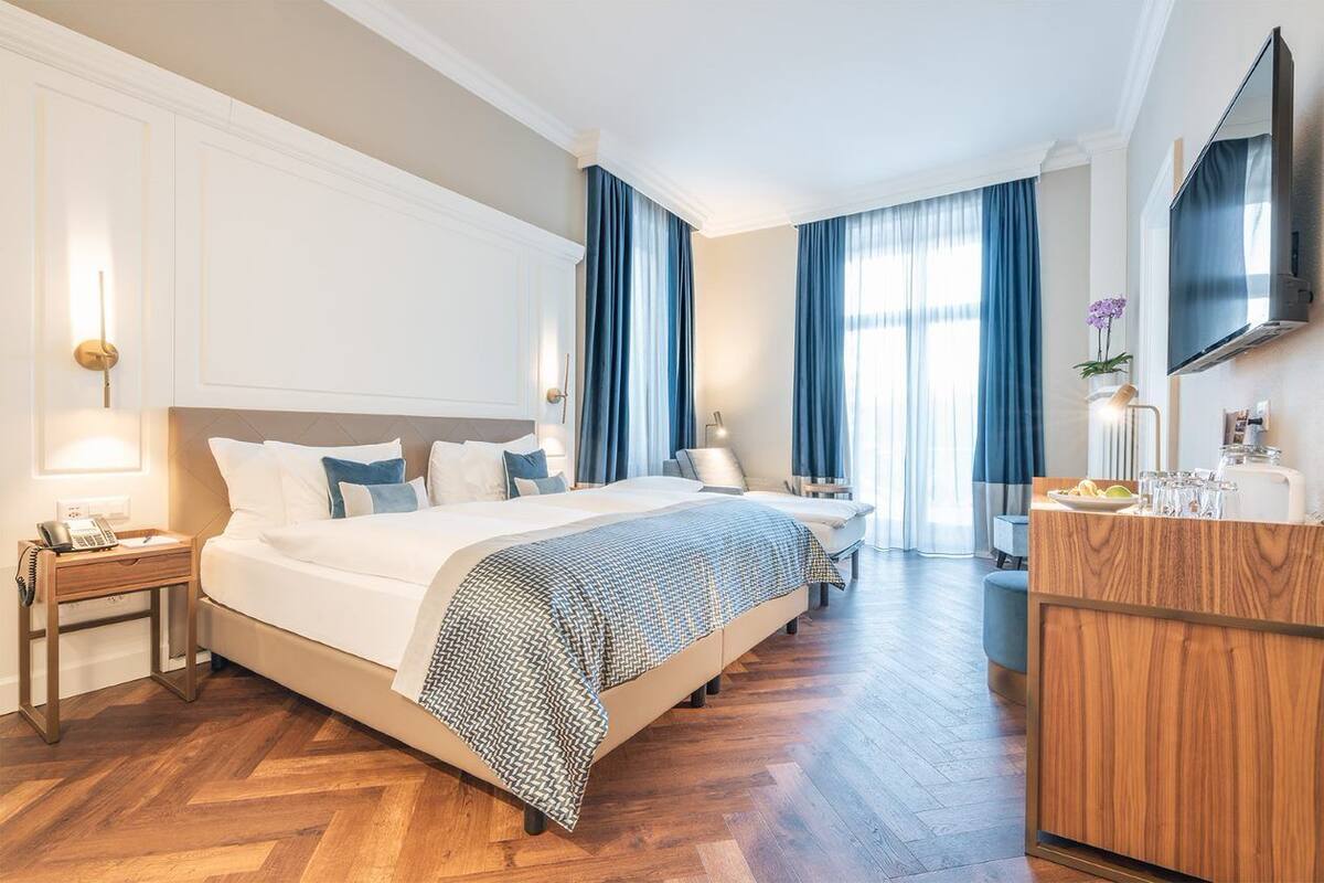 A hotel room with a large bed, a wooden dresser, a desk, and a TV mounted on the wall.