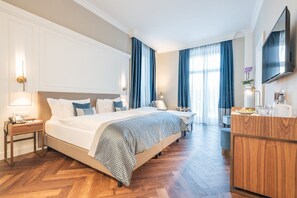 Quarto de hotel com uma cama grande, cómoda de madeira, secretária e televisão na parede.