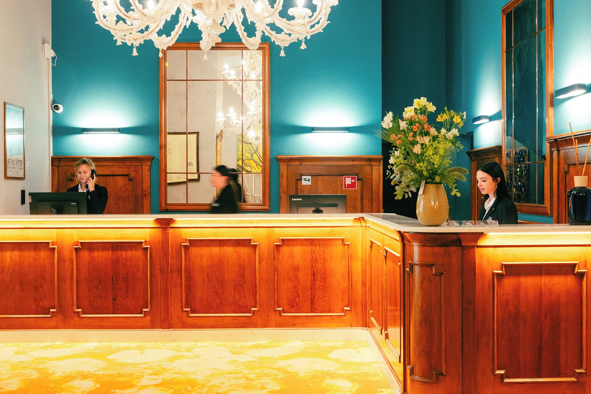 Een hotel receptie met een houten receptiebalie, een grote spiegel en een bloemenvaas.