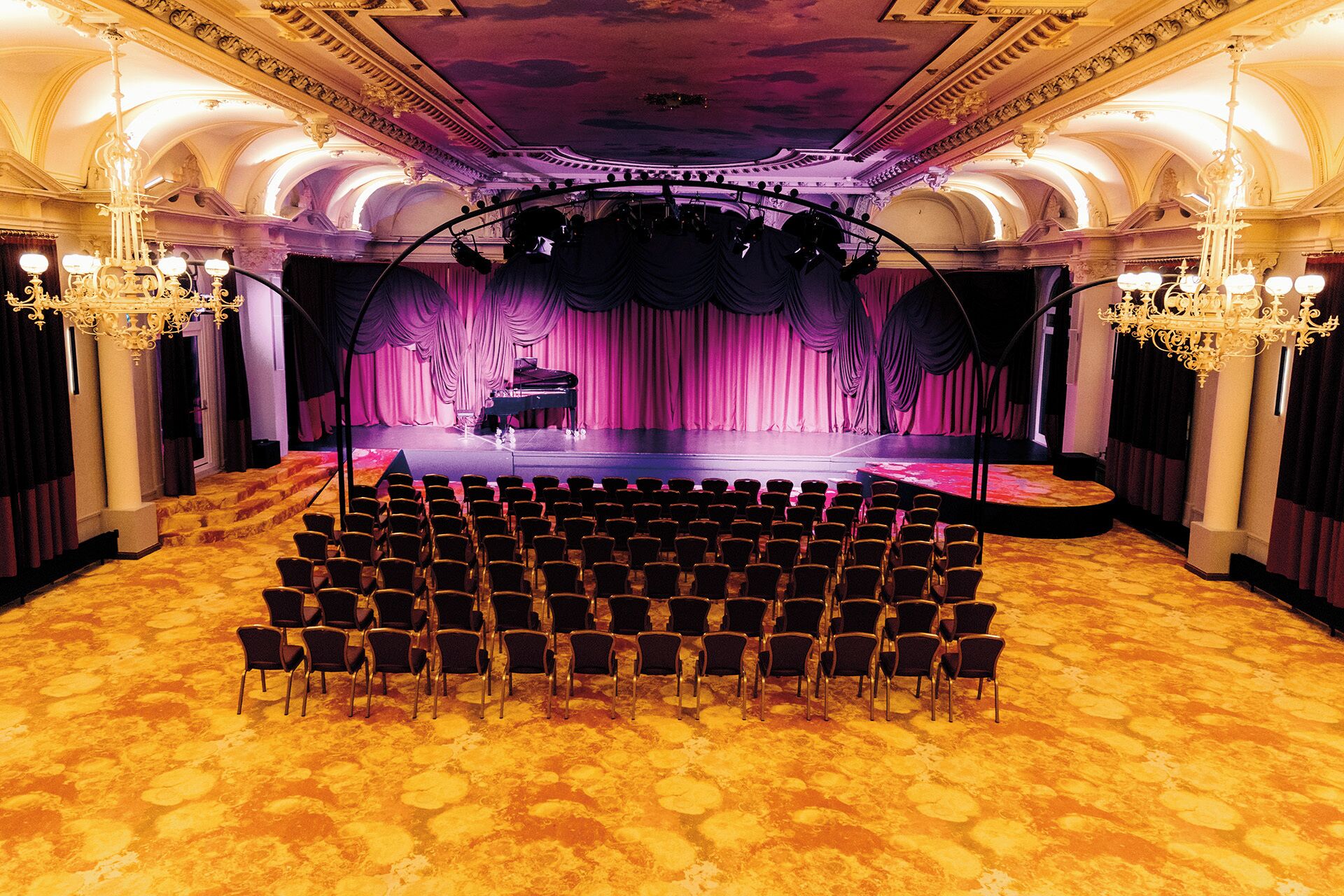 A theater with a stage, rows of chairs, and ornate chandeliers.