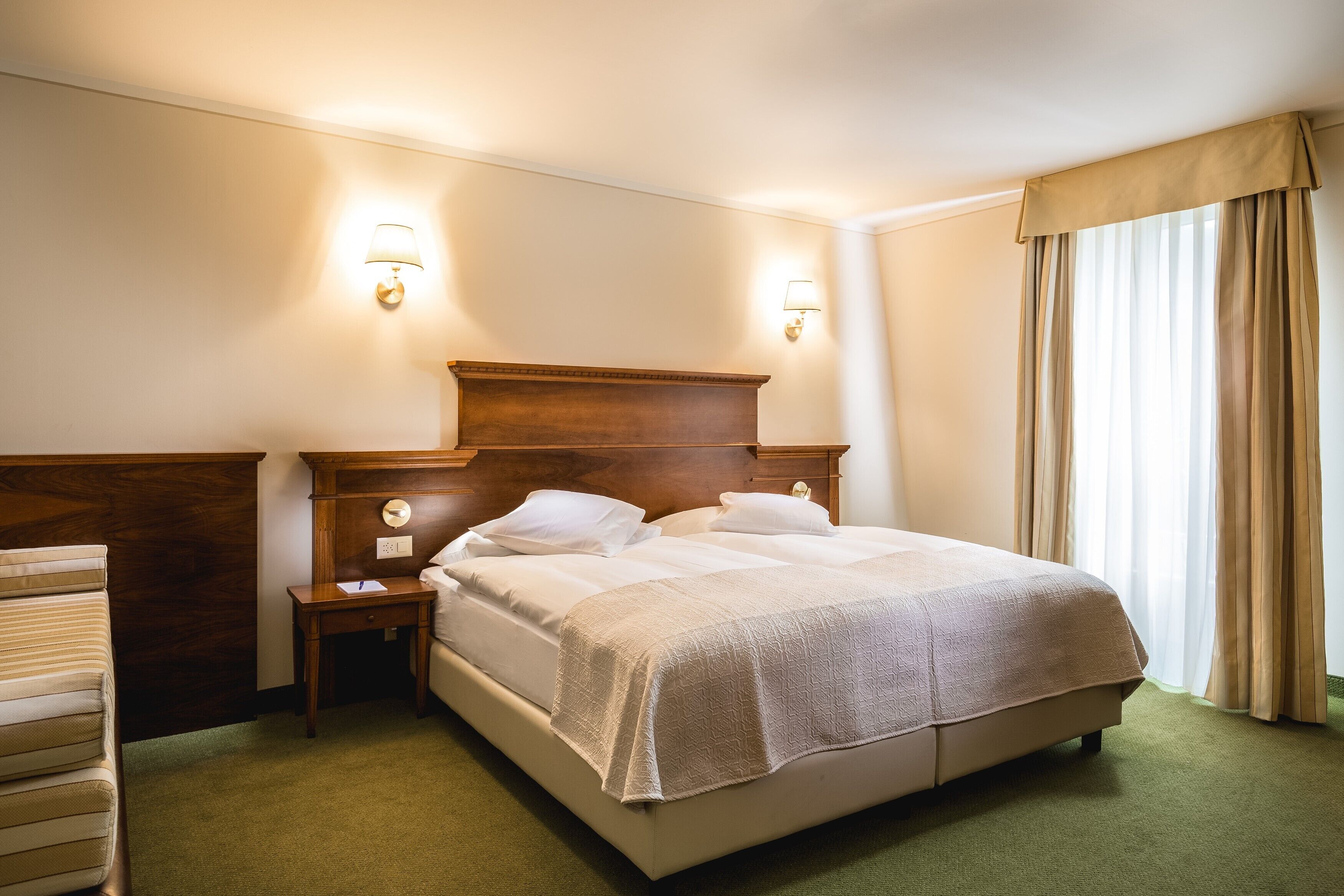 A hotel room with a large bed, two bedside tables, a nightstand, and a lamp.
