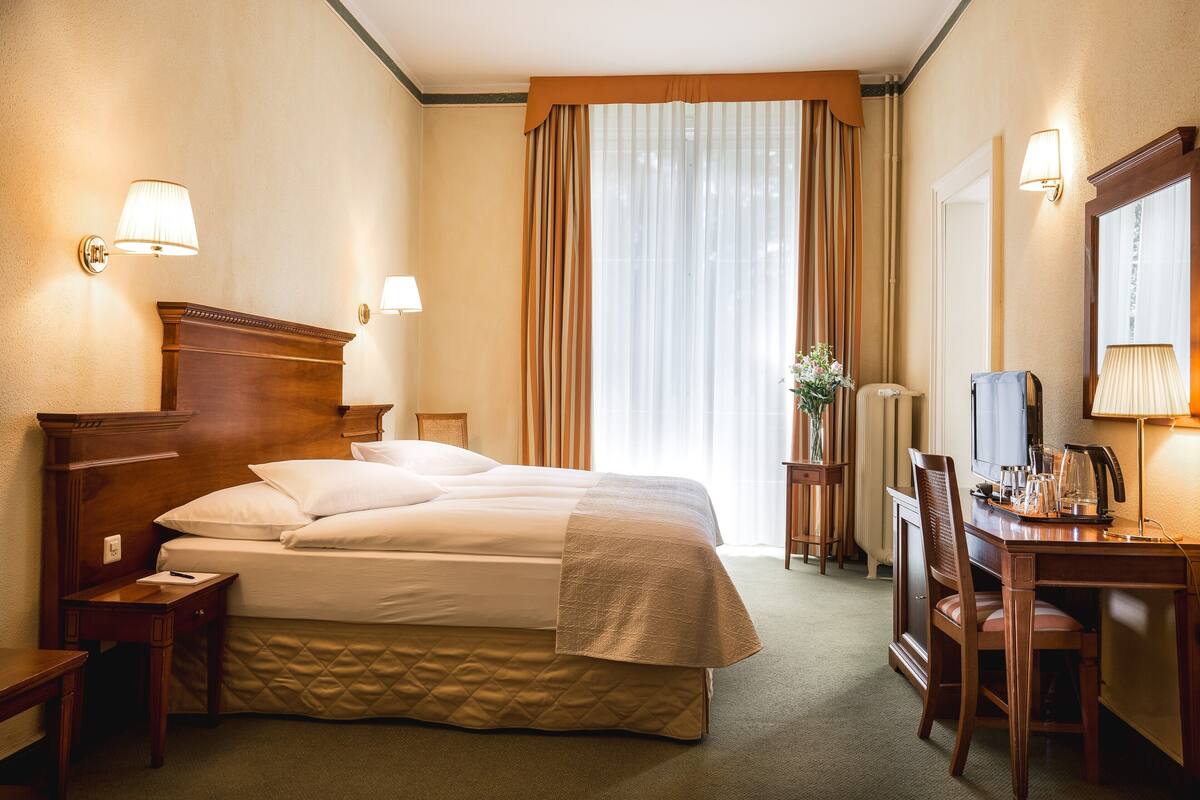A hotel room with a large bed, a desk, a chair, a lamp, and a mirror.