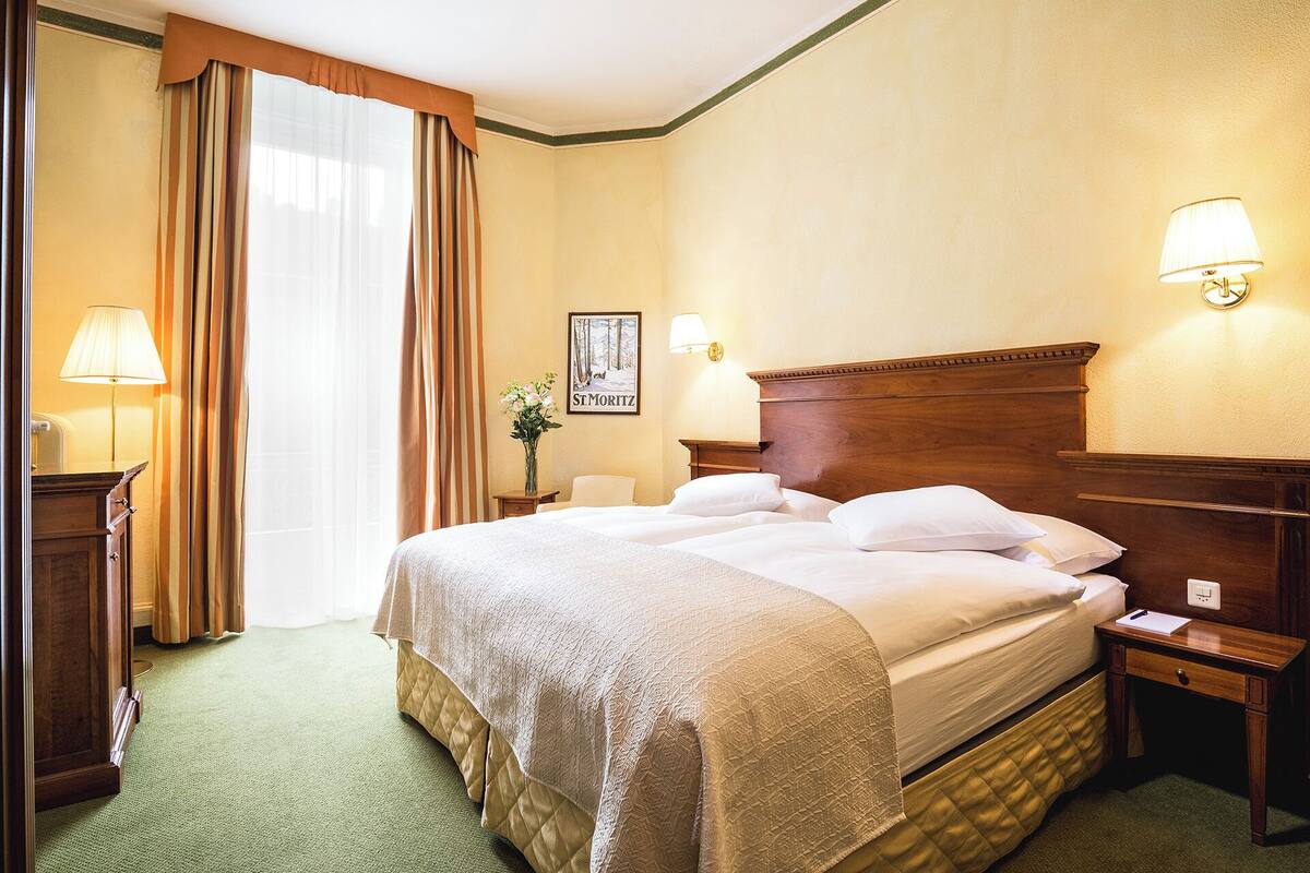 A hotel room with a large bed, two bedside lamps, a nightstand, a framed picture on the wall, and a window with curtains.