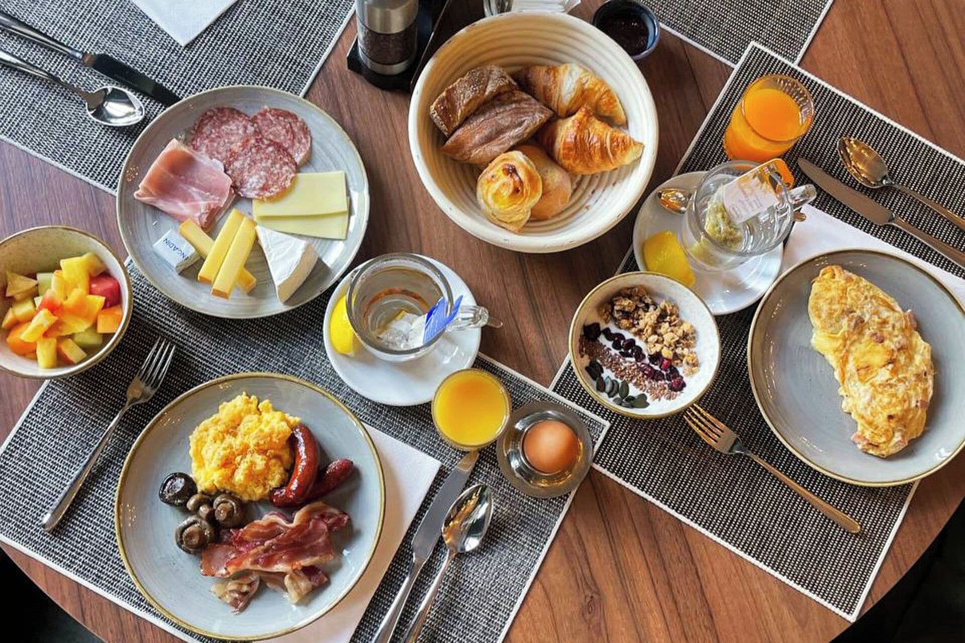 A breakfast table with plates of food, including eggs, sausages, cheese, and pastries.