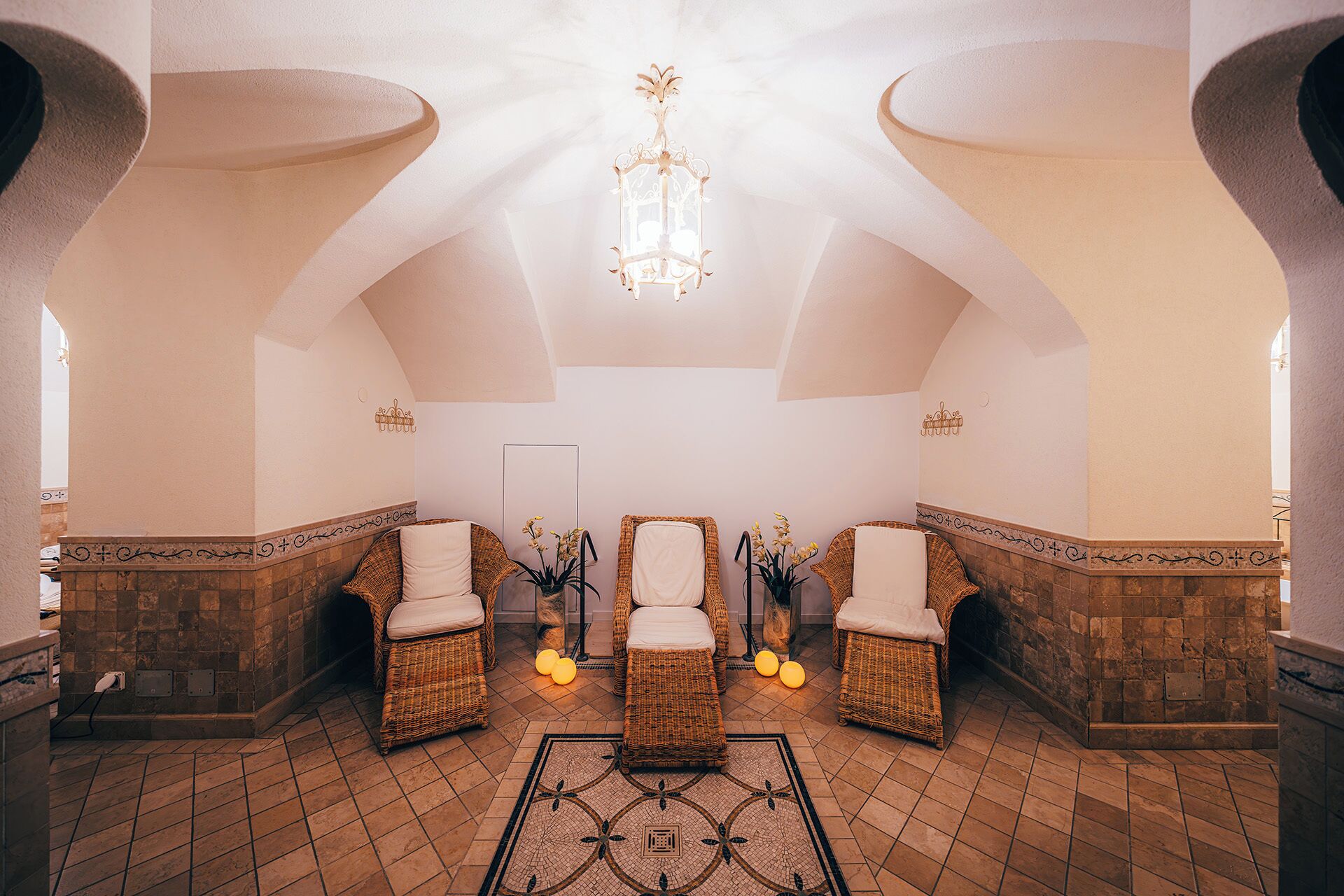 A spa room with four wicker chairs, a central chandelier, and a tiled floor.