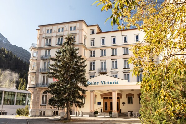 Um hotel de vários andares com estilo arquitetônico clássico, apresentando uma entrada imponente com marquise e uma placa com a inscrição "Reine Victoria".