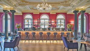 A bar area with a bartender, bar stools, and a wine and liquor display. - Hotel Reine Victoria (St. Moritz)