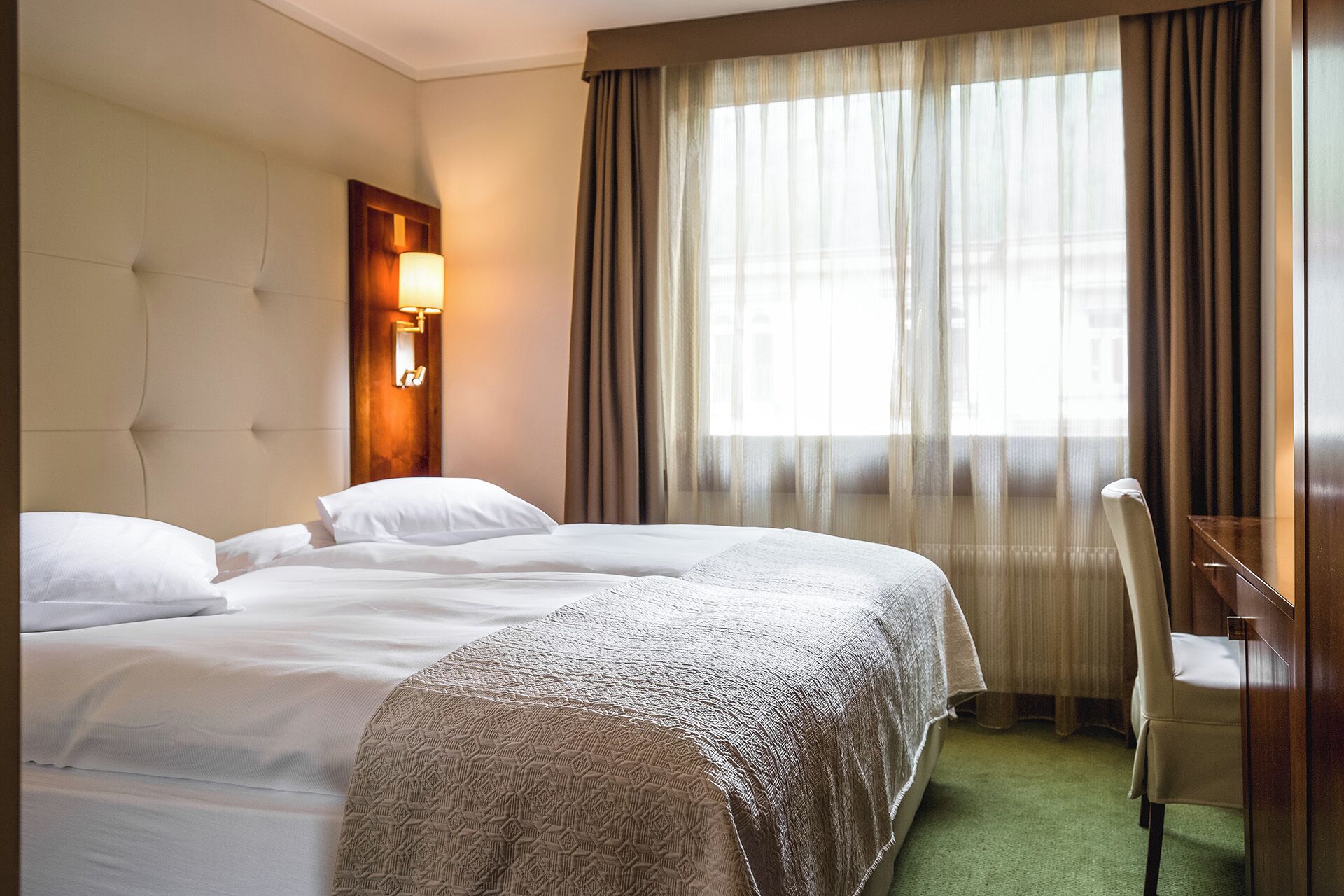 A hotel room with a large bed, a desk, and a window with curtains.