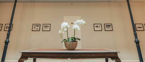 A spacious room with a high ceiling, a central table with a potted orchid, and framed pictures on the walls.