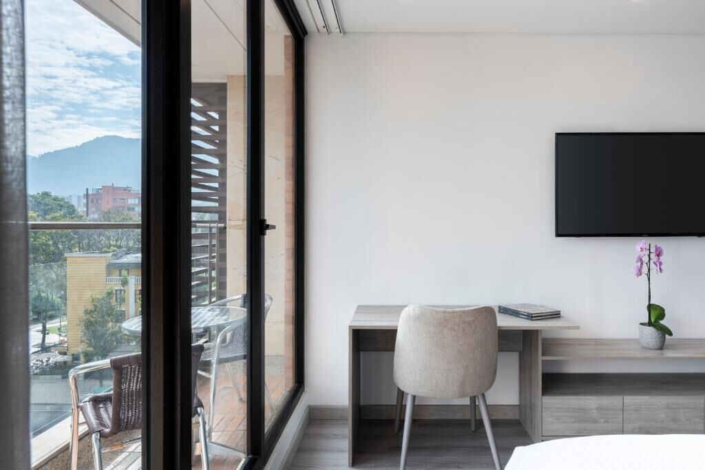 Una habitación moderna con un ventanal grande, un escritorio con una silla, un televisor de pantalla plana y una orquídea en maceta.