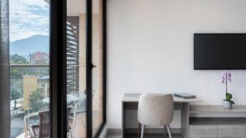Una habitación moderna con un ventanal grande, un escritorio con una silla, un televisor de pantalla plana y una orquídea en maceta.