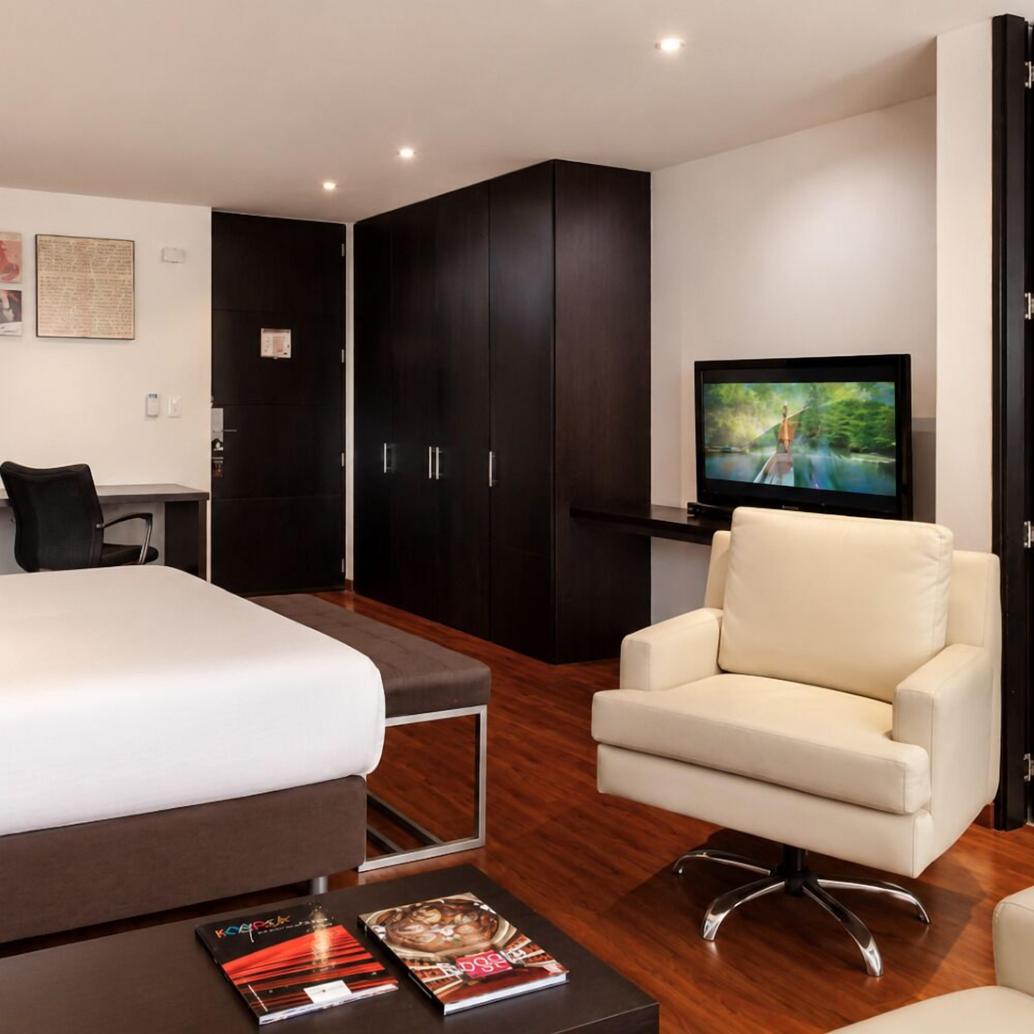 Quarto de hotel moderno com uma cama grande, televisão, escrivaninha e uma cadeira.