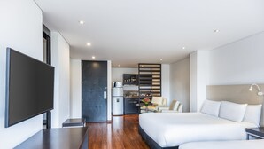 Habitació d'hotel moderna amb un llit gran, televisió, zona de cuina i espai per seure.