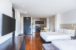 Una habitación de hotel moderna con una cama grande, televisión, kitchenette y zona de estar.
