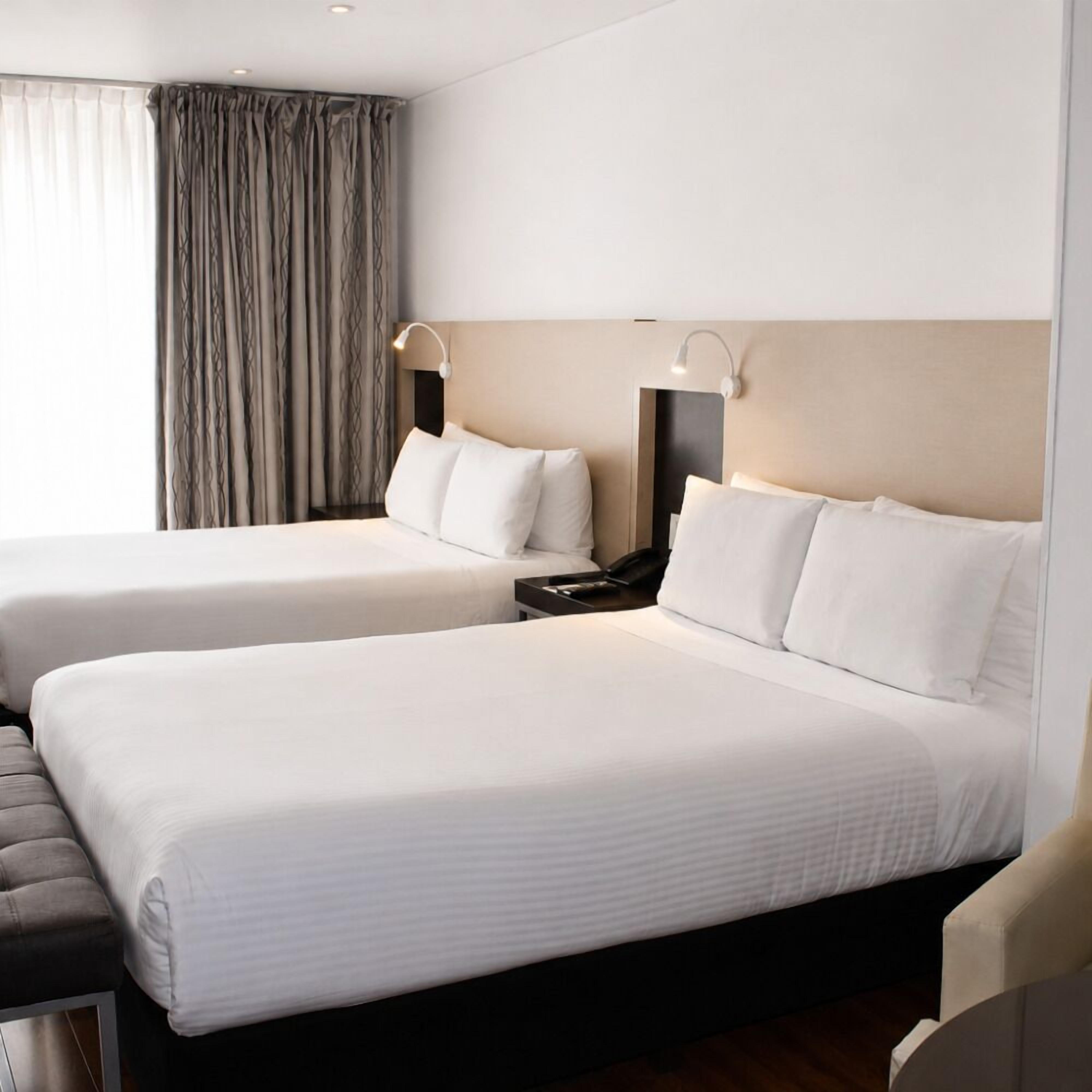 A hotel room with two beds, a desk, a chair, and a window with curtains.