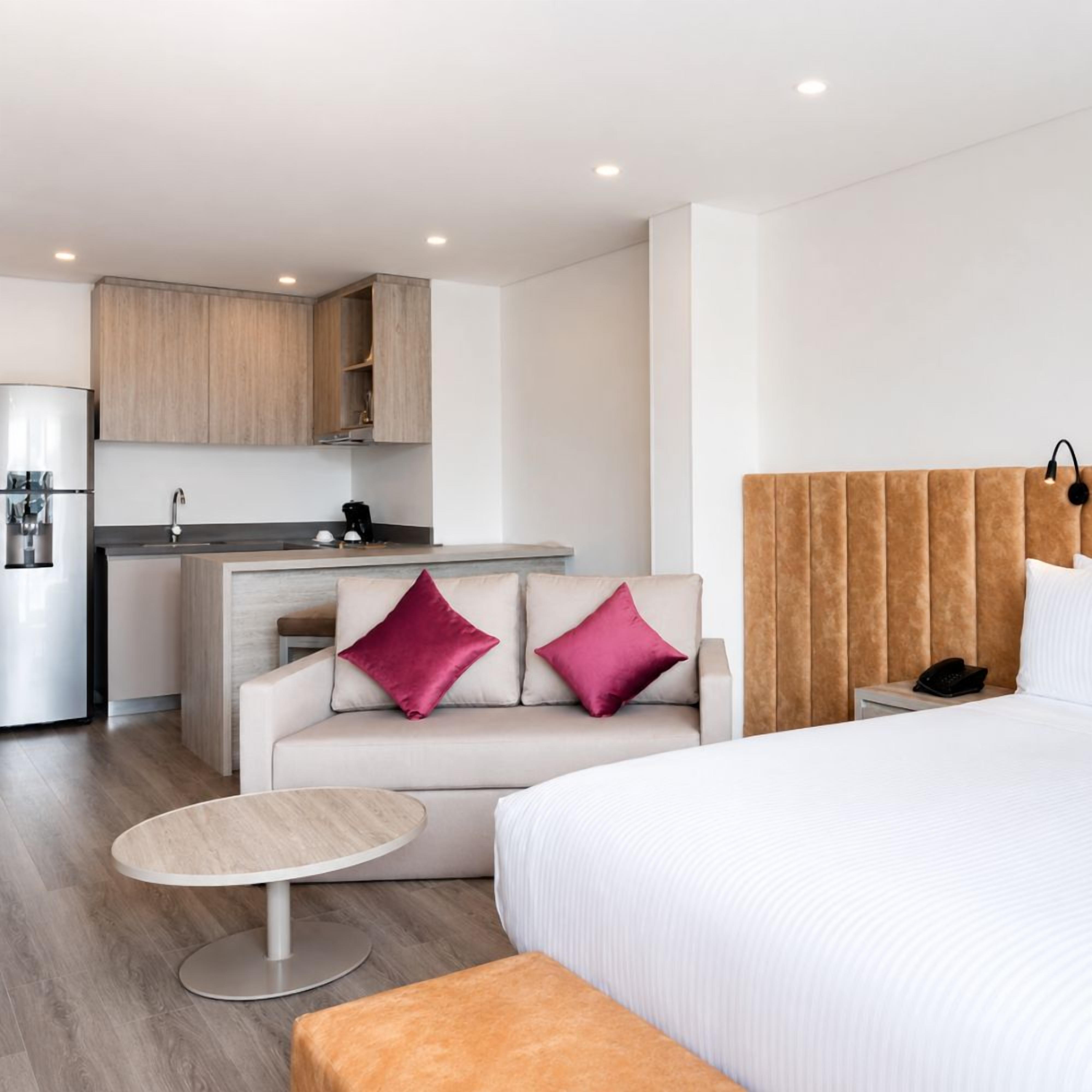 Une chambre d’hôtel moderne équipée d’un lit, d’un canapé, d’une petite table ronde et d’une kitchenette.