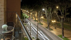Un balcó amb taula i cadires, amb vistes a un carrer ple d'arbres i fanals.