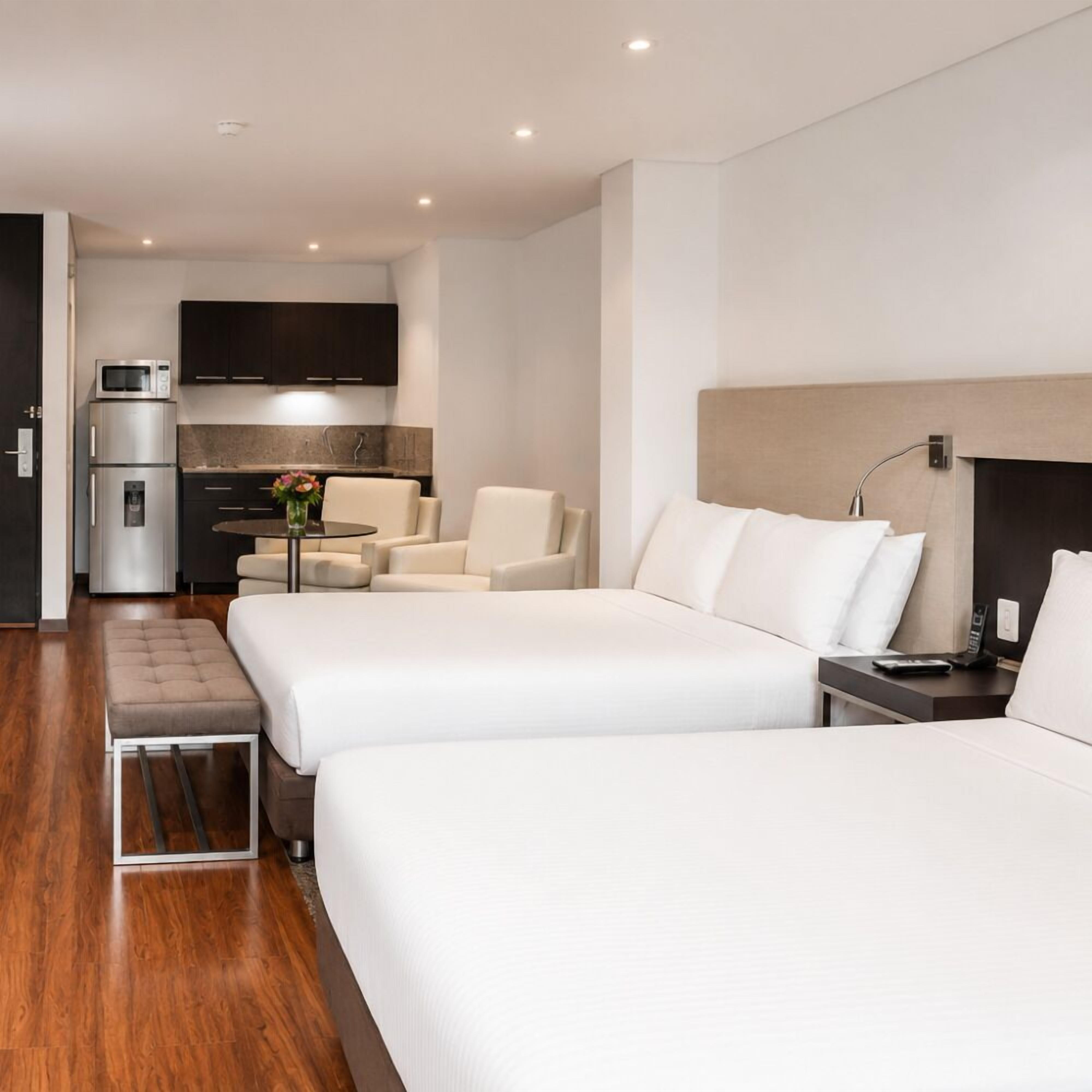 Habitación de hotel con dos camas, un kitchenette, una zona de estar y una mesita.