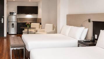 Habitación de hotel con dos camas, un kitchenette, una zona de estar y una mesita.