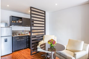Una cocina moderna con armarios oscuros, un refrigerador blanco y un separador de madera. Hay una mesa redonda con un jarrón de flores y un sillón blanco.