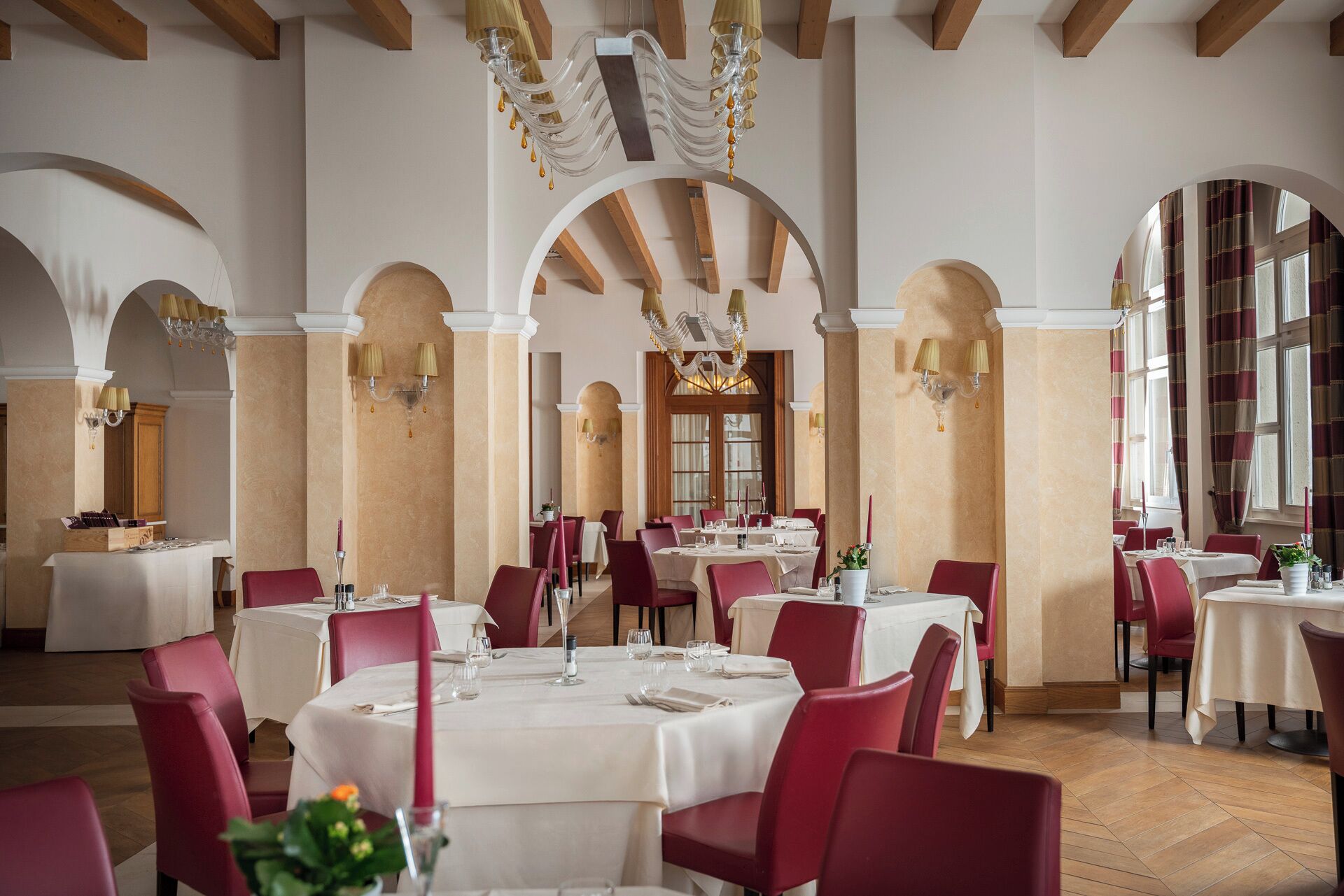 Un vaste espace dédié à la salle à manger, avec des tables rondes, des chaises rouges et un plafond haut orné de poutres en bois.