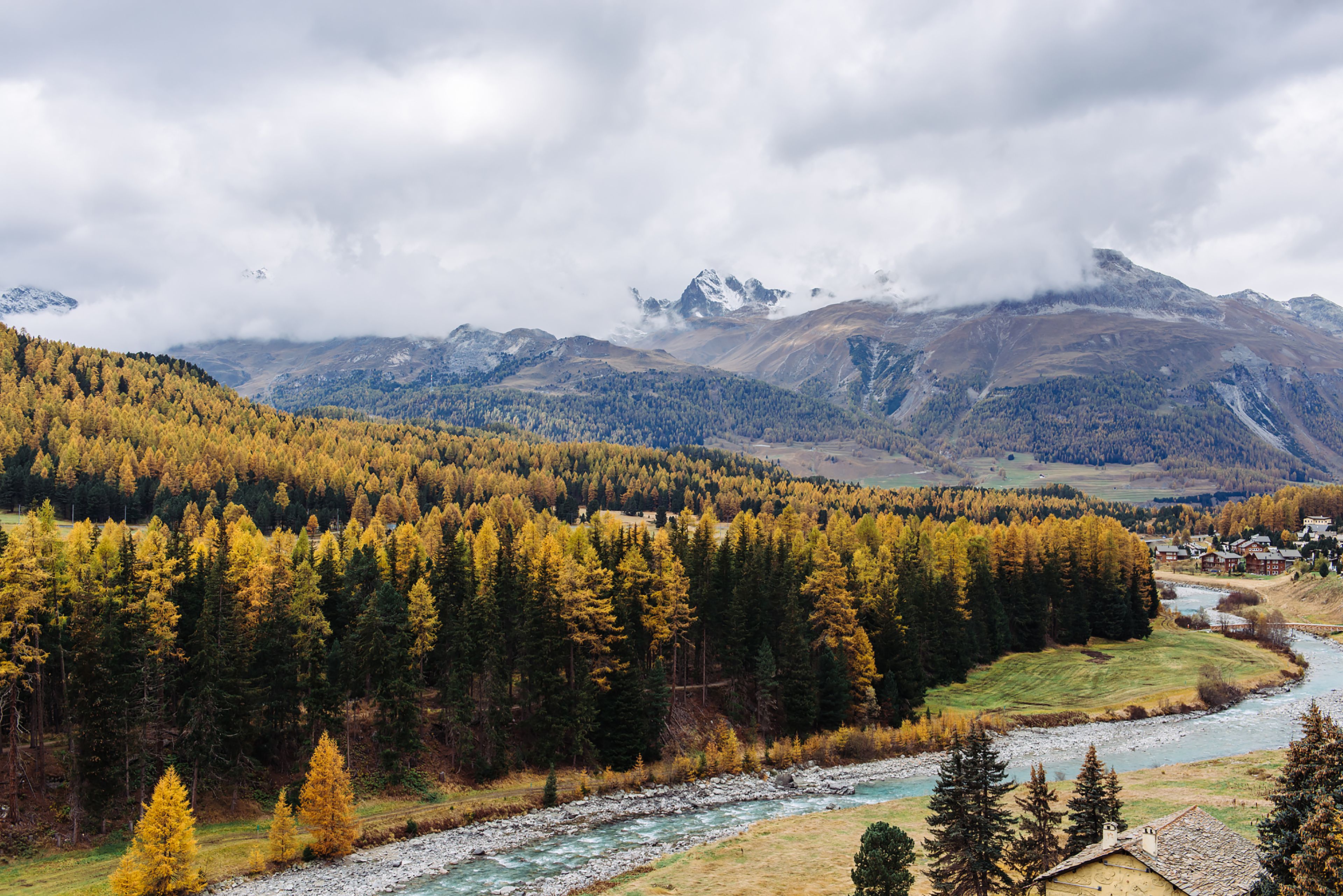 Un paisaje montañoso con un río, bosques densos y un pequeño asentamiento.