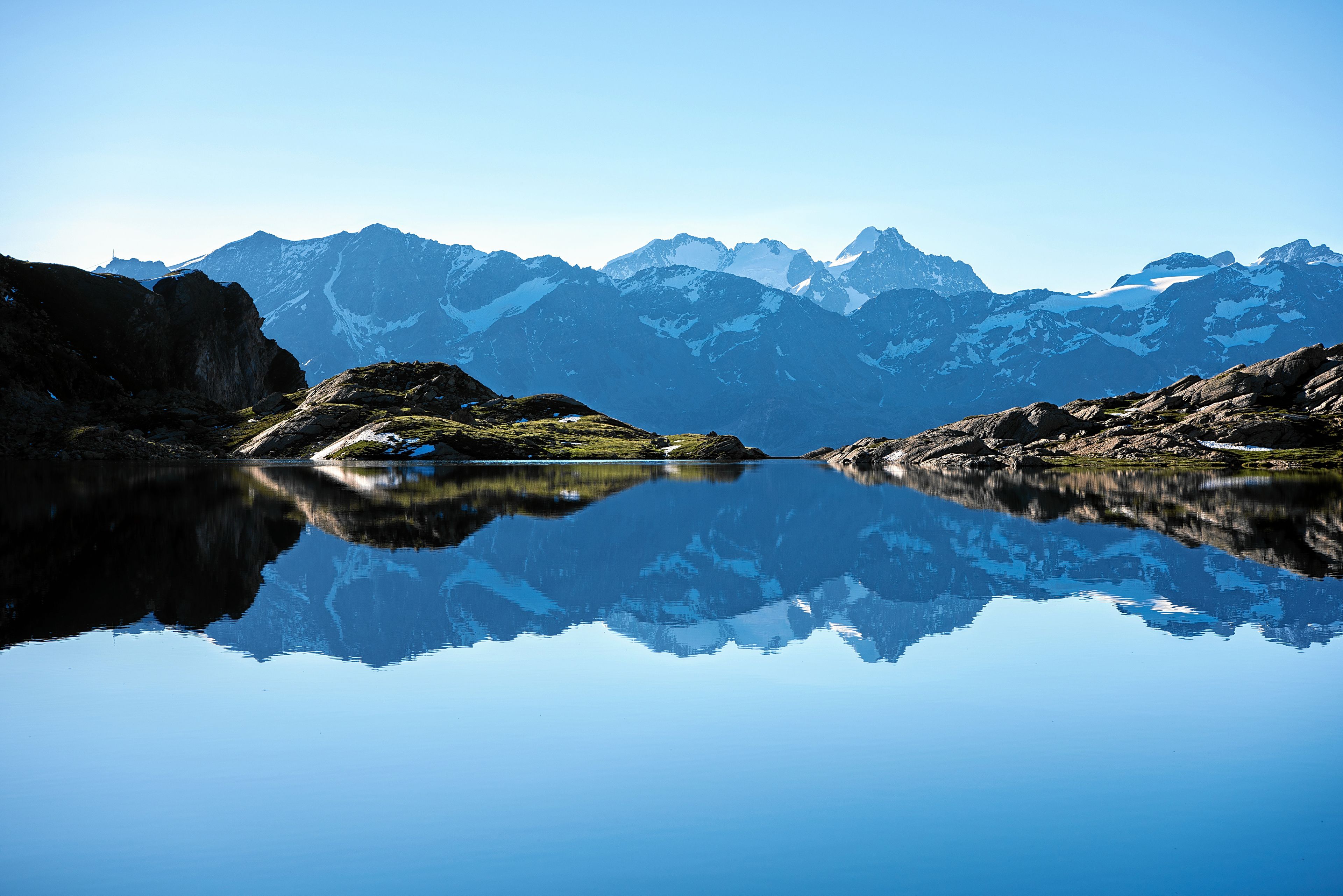 A tranquil lake reflecting mountains, surrounded by rocky terrain.