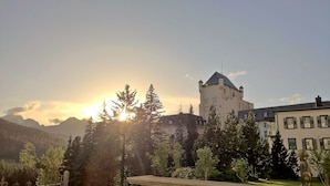 Un edificio que recuerda a un castillo, con una torre, rodeado de árboles y montañas al fondo.