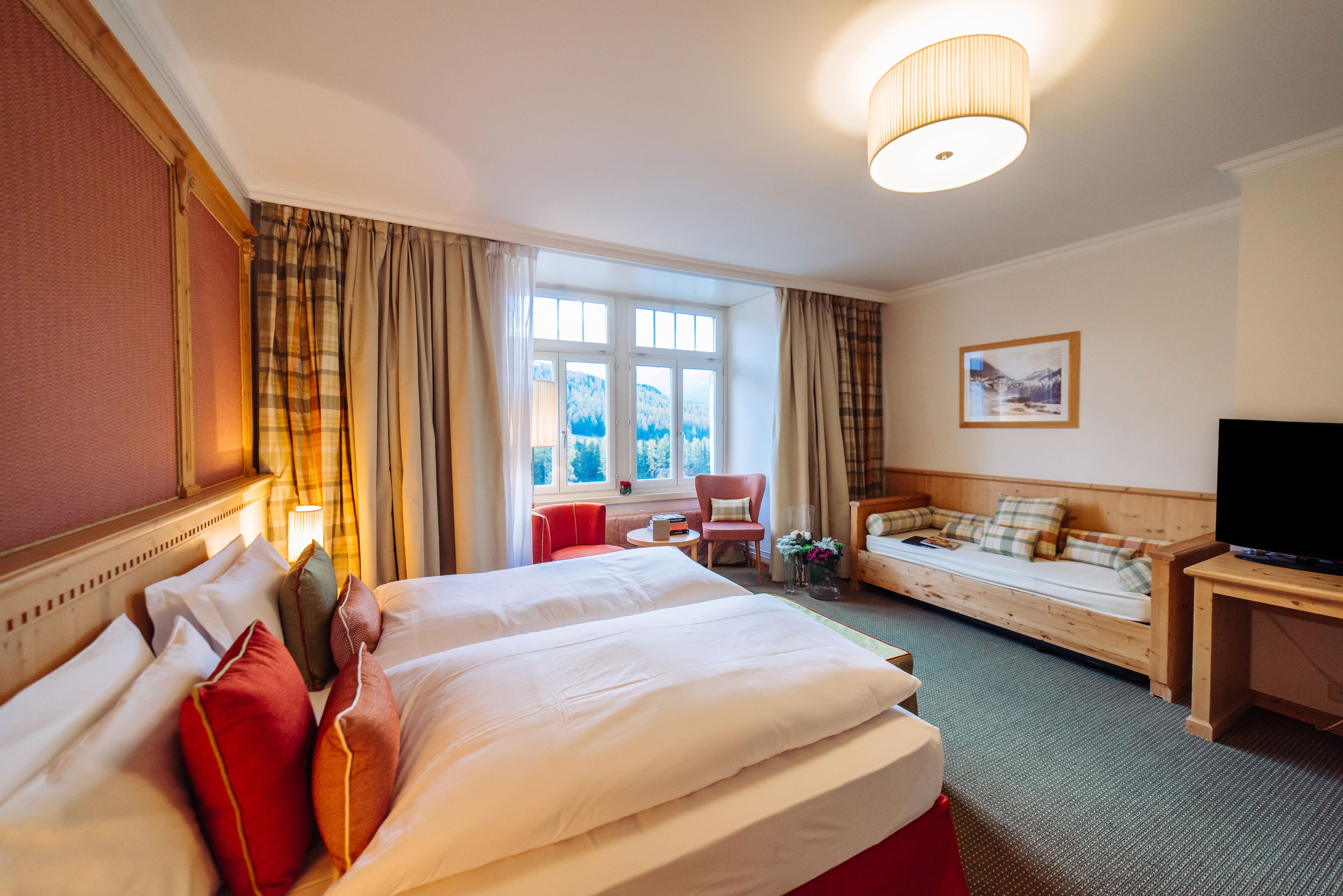 A hotel room with a large bed, a sofa, a TV, and a window with curtains.