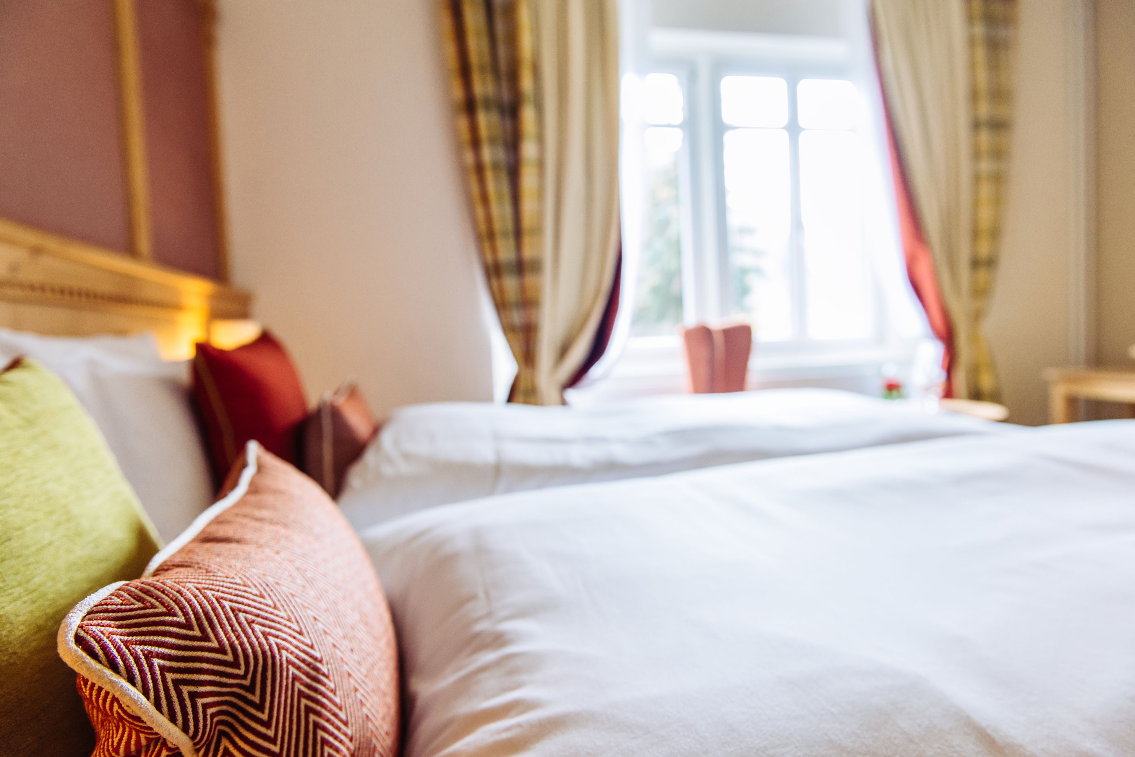 A neatly made bed with white linens and multiple pillows, including a patterned one.