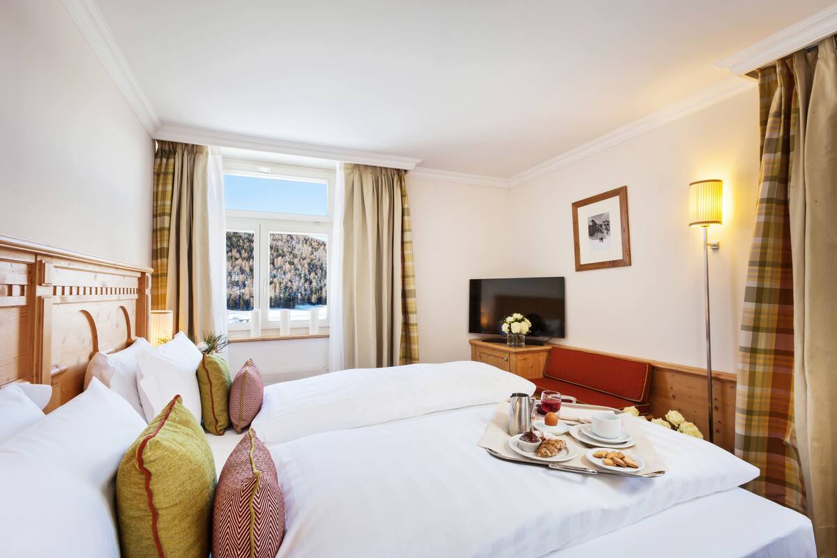 Une chambre d’hôtel avec deux lits, une télévision, une table de chevet avec une lampe et une fenêtre avec des rideaux.