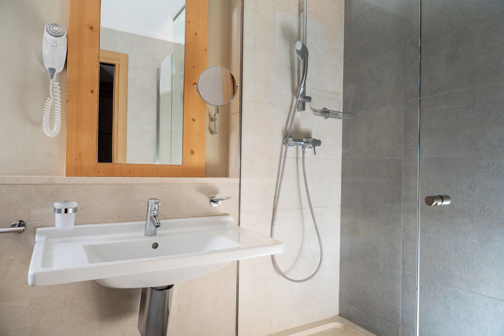 Un baño con lavamanos blanco, espejo, secador de pelo y ducha.
