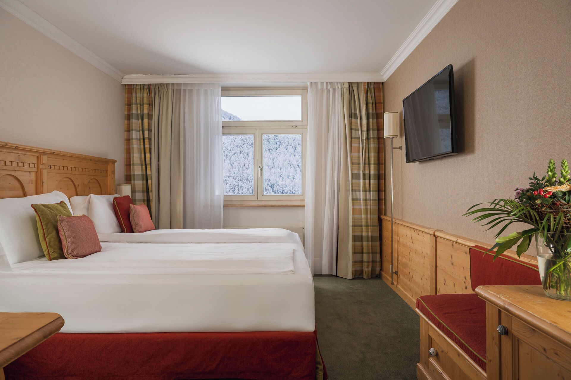 Una habitación de hotel con dos camas, una televisión, una ventana con cortinas y una pequeña mesa con una planta.