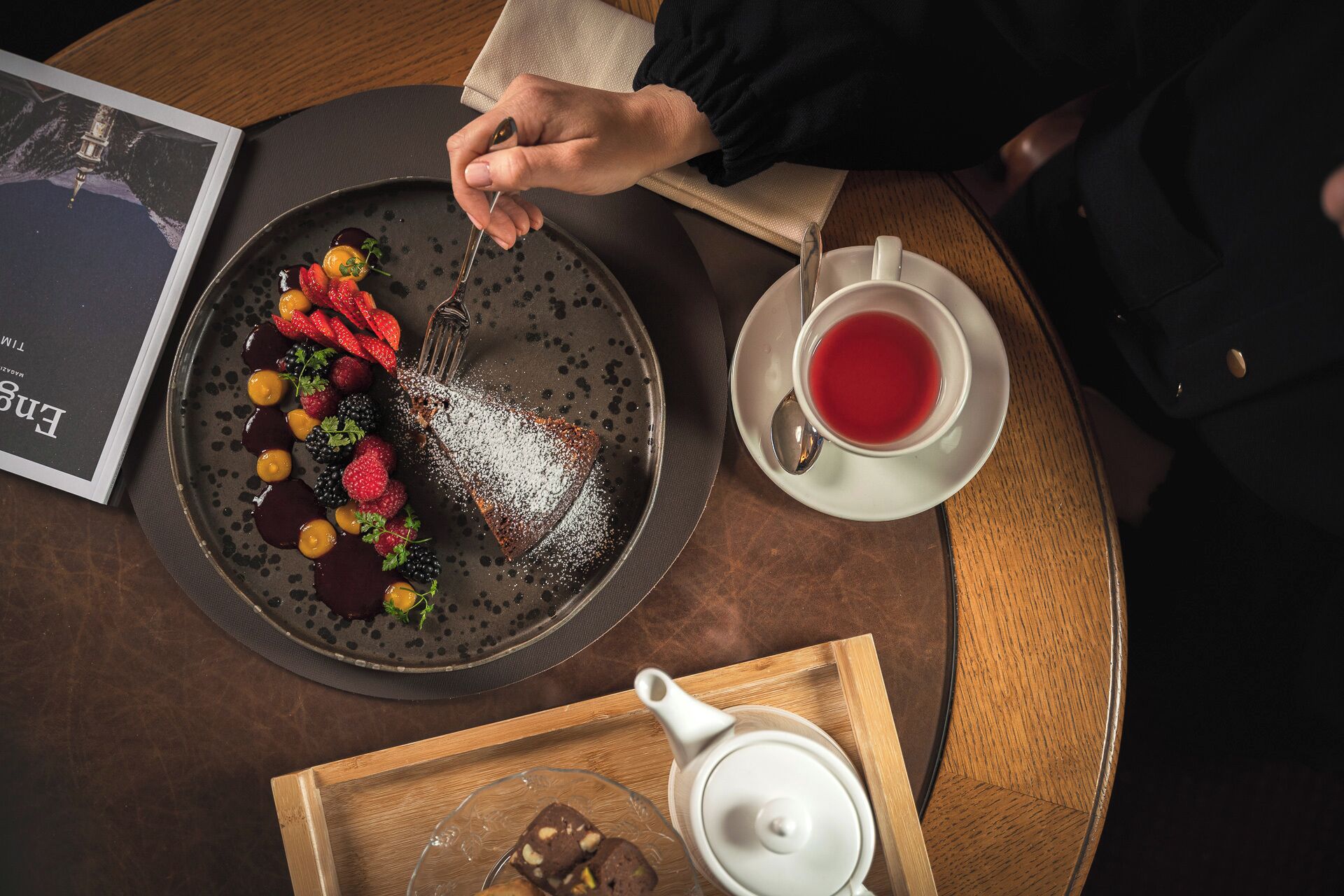 A table with a dessert plate, a teapot, and a cup of tea.