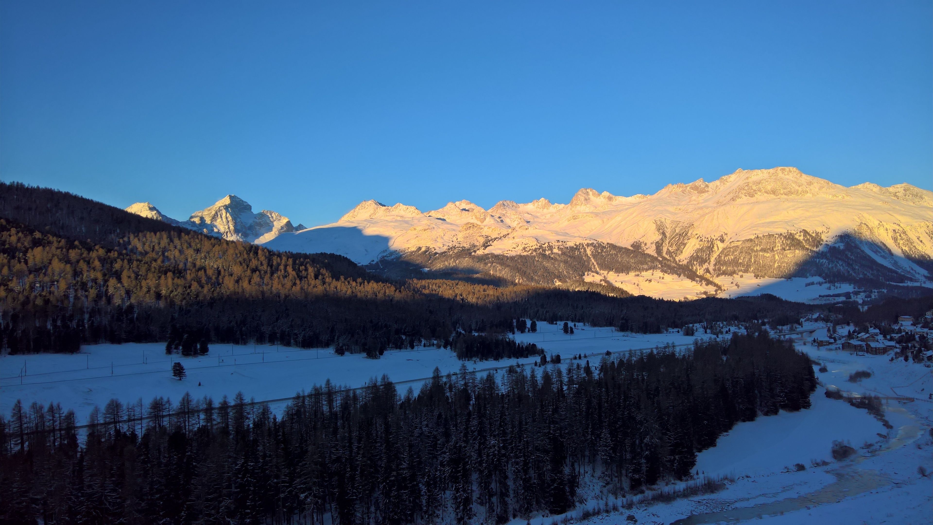 Eine gebirgige Landschaft mit schneebedeckten Gipfeln und einem bewaldeten Tal.