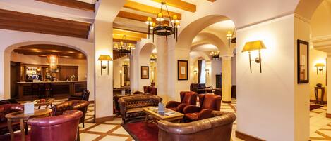 A spacious lobby with leather sofas, a coffee table, and a bar area in the background.