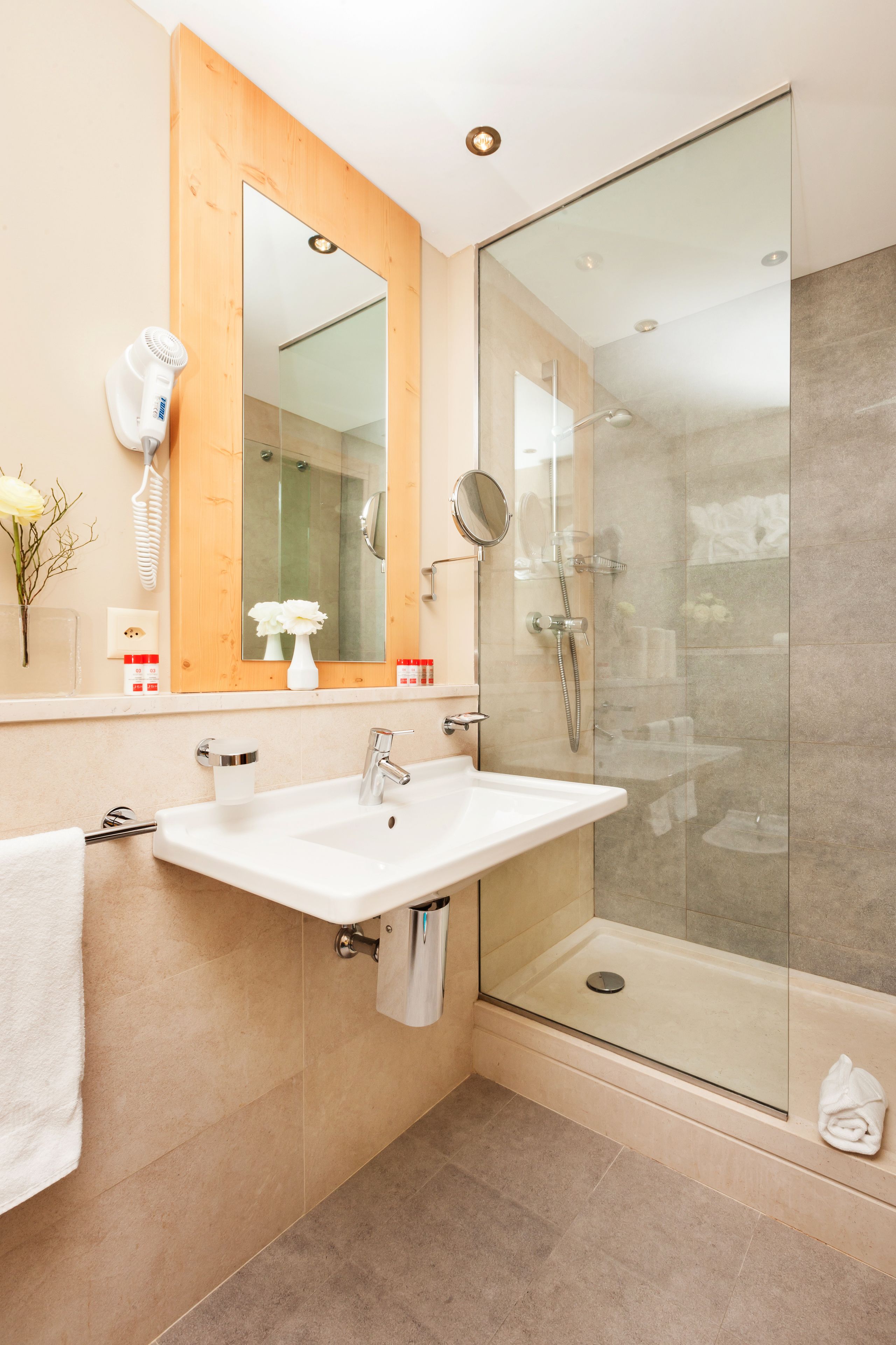 A modern bathroom with a glass-enclosed shower, a white sink, and a wooden-framed mirror.