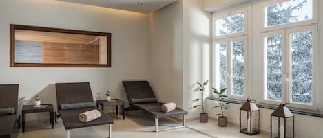 A modern lounge area with reclining chairs, a small table with a plant, and a window with a view of snow-covered trees.