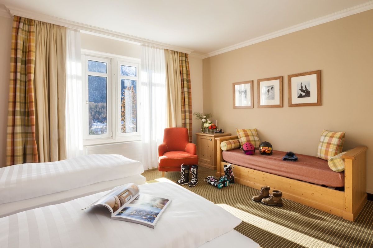 A hotel room with a bed, a sofa, a chair, and a window with curtains.