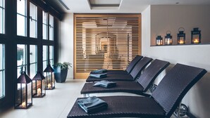 Un espacio lounge moderno con una fila de sillones negros, un separador de listones de madera y un estante en la pared con faroles.
