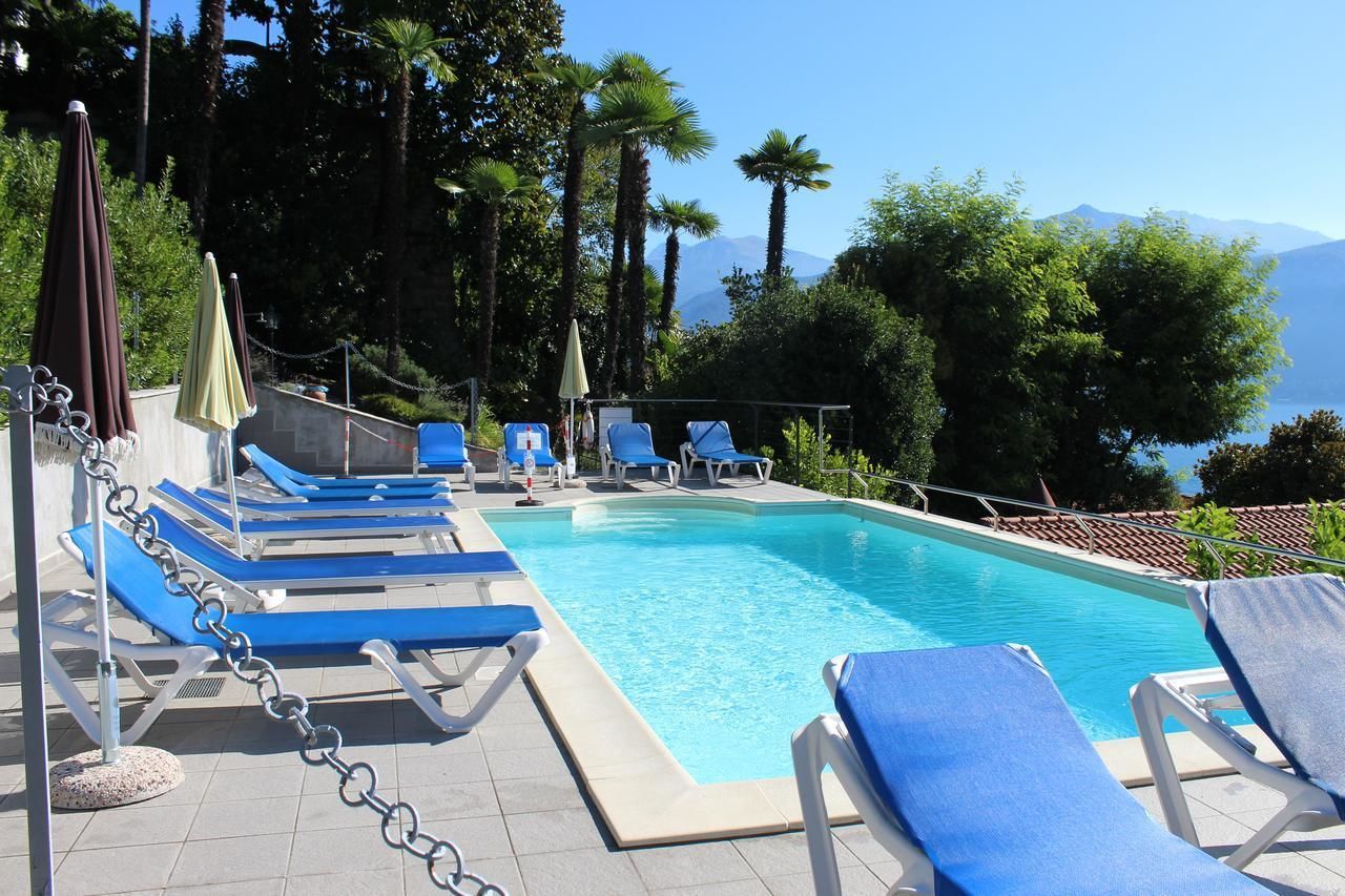 A swimming pool with blue lounge chairs and umbrellas, surrounded by trees and mountains.