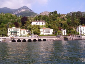 A waterfront view with a bridge, buildings, and mountains in the background. - Villa La Mirabella (Griante)