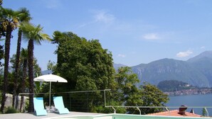 A swimming pool with lounge chairs and an umbrella, surrounded by trees and mountains in the background. - Villa La Mirabella (Griante)