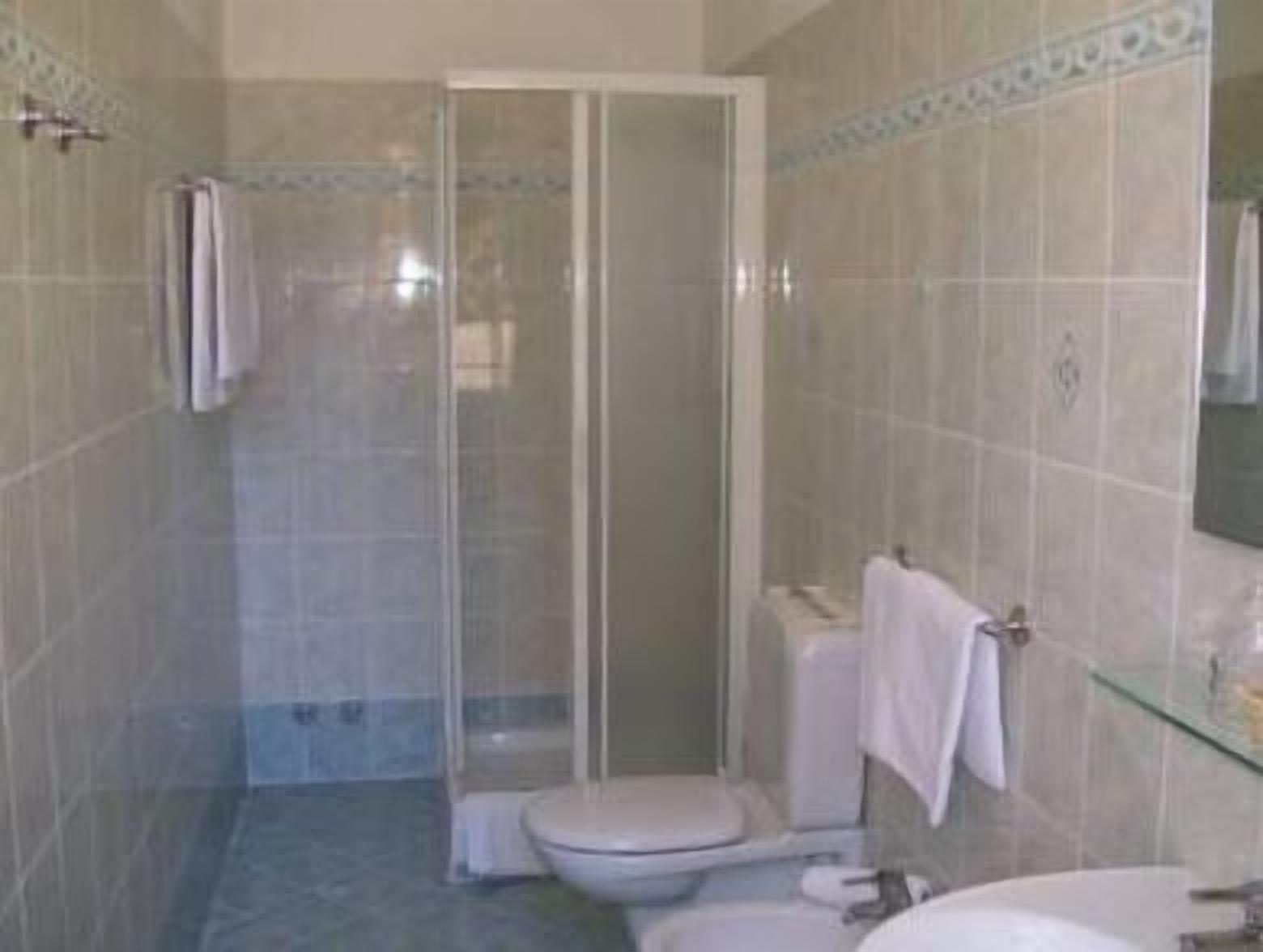A bathroom with a glass-enclosed shower, a toilet, and a sink.