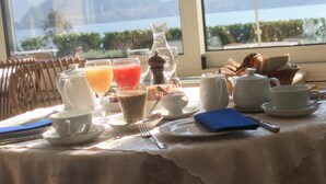 A breakfast table set with various dishes and drinks, a wicker chair, and a view of a lake through a window. - Villa La Mirabella (Griante)