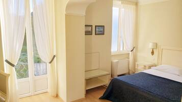 Ein Hotelzimmer mit Bett, Schreibtisch, Stuhl, einem Fenster mit Vorhängen und Blick auf Grünfläche.